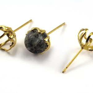 Puede incluir: Tres engastes de pendientes de tono dorado, dos con un diseño de jaula y uno con una piedra verde y negra.