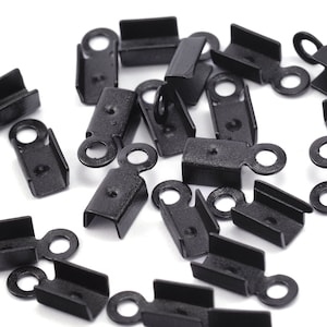 May include: A close-up of a group of black metal cord end caps with a small loop on one end. The caps are scattered on a white surface.