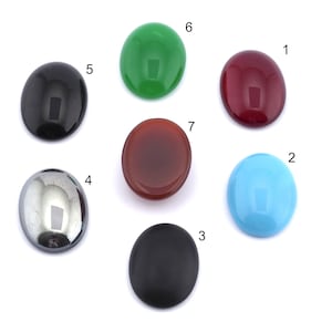Può includere: Sette cabochon ovali di vari colori, tra cui nero, verde, rosso, marrone, blu e grigio. I cabochon sono disposti in un cerchio su uno sfondo bianco.
