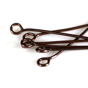 May include: A close-up of a pile of copper-colored head pins. The head pins are about 1 inch long and have a small loop at one end.