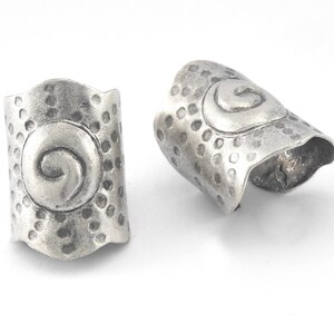May include: Two silver metal ring end caps with a swirl design and a textured surface.