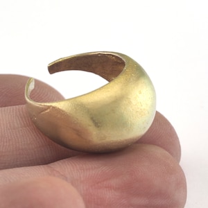 May include: A gold-colored ring with a rounded, smooth surface. The ring is open on one side and has a slightly curved shape.