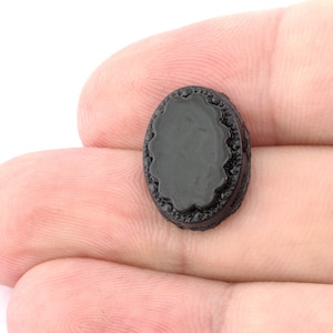 May include: A black plastic button with a decorative edge. The button is round and has a smooth surface.