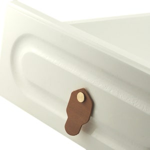May include: White drawer with a brown leather pull handle and a gold metal knob.