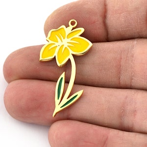 May include: Gold-tone metal charm featuring a yellow daffodil with green leaves. The charm has a loop at the top for attaching to jewelry or other crafts.