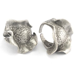 May include: Two silver rings with a textured, organic, flower-like design. The rings are open and adjustable.