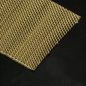 May include: Close-up of a section of gold-colored chainmail. The chainmail is made of small, interlocking rings, creating a flexible, mesh-like fabric. The background is a dark, reflective surface.