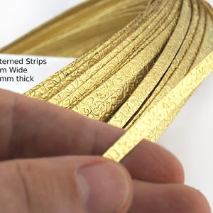 Könnte beinhalten: Nahaufnahme von goldfarbenen, gemusterten Streifen, 5 mm breit und 0,8 mm dick, mit strukturierter Oberfläche. Die Streifen sind zu einer Rolle aufgerollt. Der Text "Patterned Strips 5mm Wide 0,8mm thick" ist sichtbar.