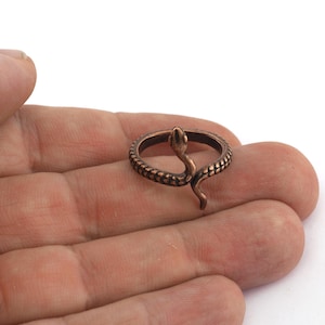 Könnte beinhalten: Ein bronzefarbener Ring mit Schlangenmotiv. Der Ring hat ein strukturiertes Band und eine Schlange, die sich um den Finger windet. Der Kopf der Schlange ist erhoben und ihr Körper ist nach unten gebogen. Der Ring ist ein Schmuckstück.