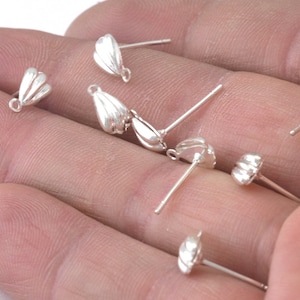 May include: Silver earring findings with a teardrop shape. The findings are shown on a hand.
