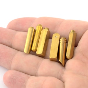 May include: A collection of six gold-colored metal rods of varying lengths, arranged in a row on a hand.