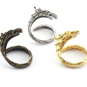 May include: Three dragon head rings in silver, gold, and bronze. The rings are open and have a dragon head design.