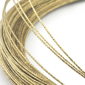 May include: A close-up of a spool of gold-colored wire with a textured surface. The wire is coiled tightly and has a shiny finish.
