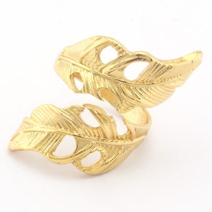 May include: A gold-toned ring featuring a double feather design. The feathers are intricately detailed and have a cutout pattern.
