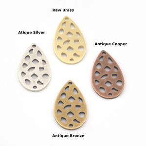 May include: Four metal teardrop-shaped charms with a cutout design. The charms are in raw brass, antique silver, antique copper, and antique bronze.