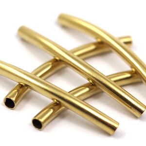 May include: Four gold-colored metal tubes, each bent into a gentle curve. The tubes are arranged in a criss-cross pattern, with the ends of each tube visible.