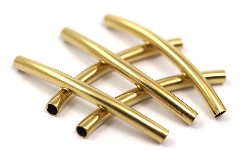 May include: Four gold-colored metal tubes, each bent into a gentle curve. The tubes are arranged in a criss-cross pattern, with the ends of each tube visible.