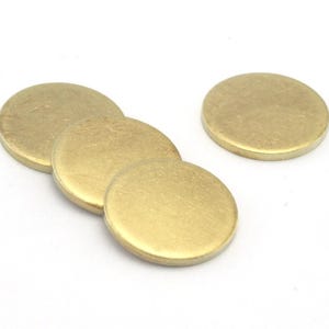 Op de afbeelding: Een verzameling van vijf kleine, ronde metalen schijven in messingkleur. De schijven liggen op een witte achtergrond en overlappen elkaar enigszins. De oppervlakken zijn glad en reflecterend, met een subtiele gouden tint.