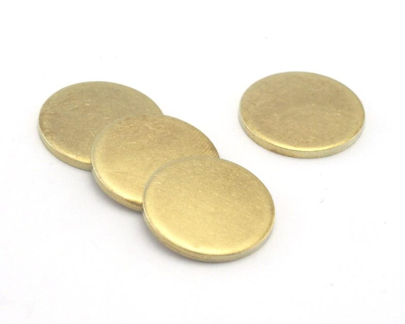 Op de afbeelding: Een verzameling van vijf kleine, ronde metalen schijven in messingkleur. De schijven liggen op een witte achtergrond en overlappen elkaar enigszins. De oppervlakken zijn glad en reflecterend, met een subtiele gouden tint.