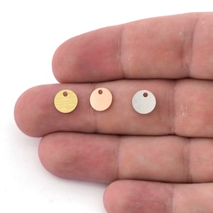 Puede incluir: Tres dijes redondos de metal con un agujero en la parte superior. Los dijes son de oro, oro rosa y plata.