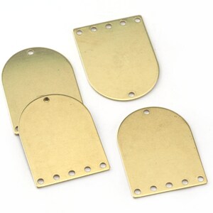 Puede incluir: Cuatro etiquetas metálicas doradas con tapas redondeadas y agujeros para sujetar artículos. Tres de las etiquetas tienen un borde inferior recto con cinco agujeros, mientras que la cuarta etiqueta tiene un borde inferior redondeado con un solo agujero.