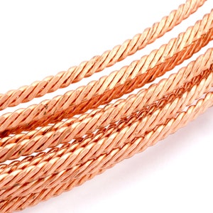 May include: Close-up of a bundle of copper wire, twisted together in a rope-like pattern. The wire is a warm, reddish-brown color.