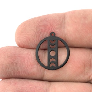 May include: Black metal charm with a circle design featuring a vertical line with crescent moon cutouts.