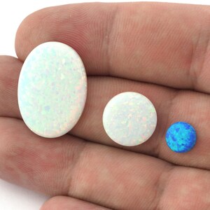 May include: Four opal cabochons in various sizes and shapes. The largest is an oval, the next two are round, and the smallest is a round blue opal.