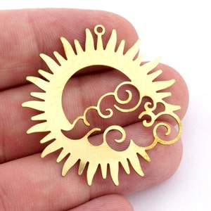 Könnte beinhalten: Goldener Metall-Sonnen- und Wolkenanhänger mit einem Ausschnittmuster. Die Sonne hat einen Kreis in der Mitte mit Strahlen, die nach außen verlaufen. Die Wolke ist mit Wirbeln stilisiert.