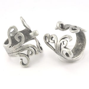 May include: Two silver rings with a swirling, ornate design. The rings are open and have a simple, rounded band.