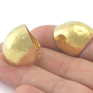 May include: Two gold-toned, hammered metal rings. The rings are open and have a rounded, dome-like shape.
