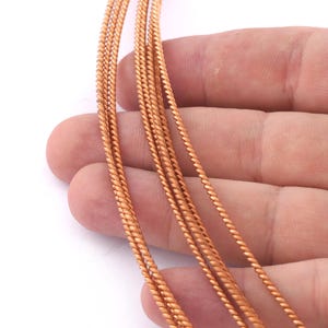 Peut inclure: Gros plan sur cinq brins de fil de cuivre, chacun avec une texture torsadée en forme de corde. Le fil est de couleur brun rougeâtre chaud.