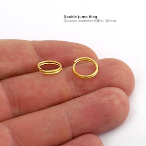 May include: Two gold-colored double jump rings, each with an outside diameter of 10mm, are displayed. The rings are held in a hand against a white background. The text "Double Jump Ring Outside diameter (OD) : 10mm" is visible.