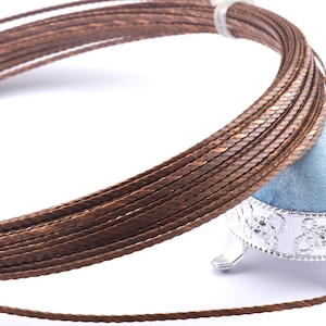 May include: A spool of brown braided copper wire. The wire is wound around a small, silver-coloured stand with three legs.
