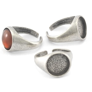 Op de afbeelding: Drie zilveren ringen met ronde bezels. Een ring heeft een bruine steen in de bezel. De andere twee ringen hebben lege bezels.