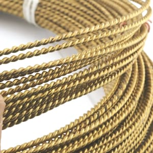 Könnte beinhalten: Nahaufnahme einer Spule mit goldfarbenem, gedrehtem Draht. Der Draht ist fest gewickelt und hat eine glänzende, metallische Oberfläche.