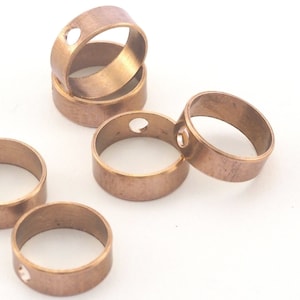 Könnte beinhalten: Sechs goldfarbene Metallringe mit einem kleinen Loch in jedem. Die Ringe sind übereinander gestapelt.