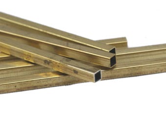 May include: Close-up of several brass square tubes, arranged in a slightly overlapping pattern. The tubes have a golden color and a hollow, square interior. The ends of the tubes are visible, showing the square opening. The background is plain white.