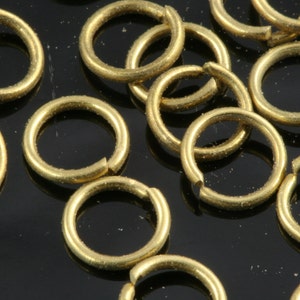 May include: A close-up of a pile of gold jump rings. The rings are small and round, and they are all made of the same metal.