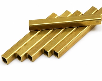 May include: A collection of six metallic brass square tubes arranged in a parallel stack with one tube placed horizontally across the others. Each tube features a hollow square cross-section and a smooth, reflective gold-toned surface finish.