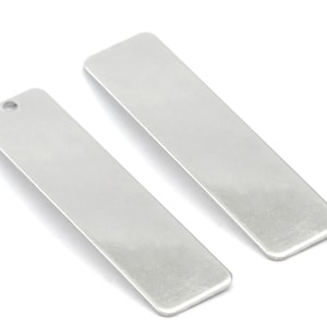 Könnte beinhalten: Zwei rechteckige silberne Metalletiketten mit einem Loch oben. Die Etiketten sind leer und bereit zur Personalisierung.