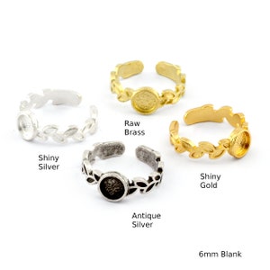 Può includere: Quattro anelli regolabili con un design a foglia e una lunetta vuota da 6 mm. Gli anelli sono mostrati in ottone grezzo, argento lucido, argento antico e oro lucido.