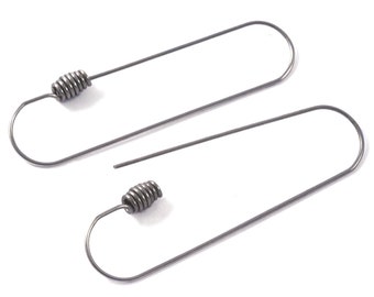 Puede incluir: Un par de pendientes de plata con un diseño en espiral. Los pendientes están hechos de metal fino y tienen un aspecto simple y moderno.