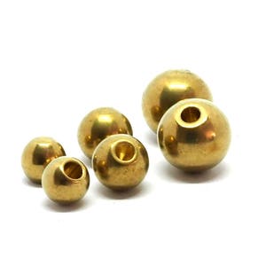 May include: Assortment of gold-coloured metal beads of varying sizes. The beads have a smooth, shiny finish and a hole in the centre.