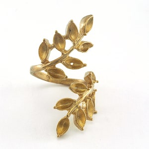 Puede incluir: Un anillo de color dorado con un diseño de hojas. El anillo está hecho de metal y tiene un diseño delicado e intrincado.