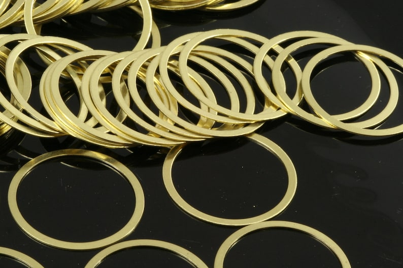 May include: A pile of gold-colored metal rings, some stacked on top of each other, on a black background.