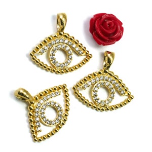 May include: Three gold-tone eye-shaped pendants with clear rhinestone accents. Each pendant has a loop at the top for attaching to a chain or cord.