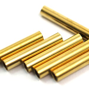 May include: A group of six gold-colored metal tubes, arranged in a staggered pattern on a white surface.