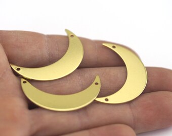 Puede incluir: Tres formas de media luna de metal dorado con dos agujeros cada una. Las formas de luna están sobre una mano.