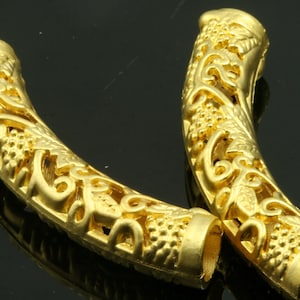 Puede incluir: Dos tapas de cuentas de metal dorado con un intrincado diseño floral. Las tapas son huecas y tienen una forma redondeada.